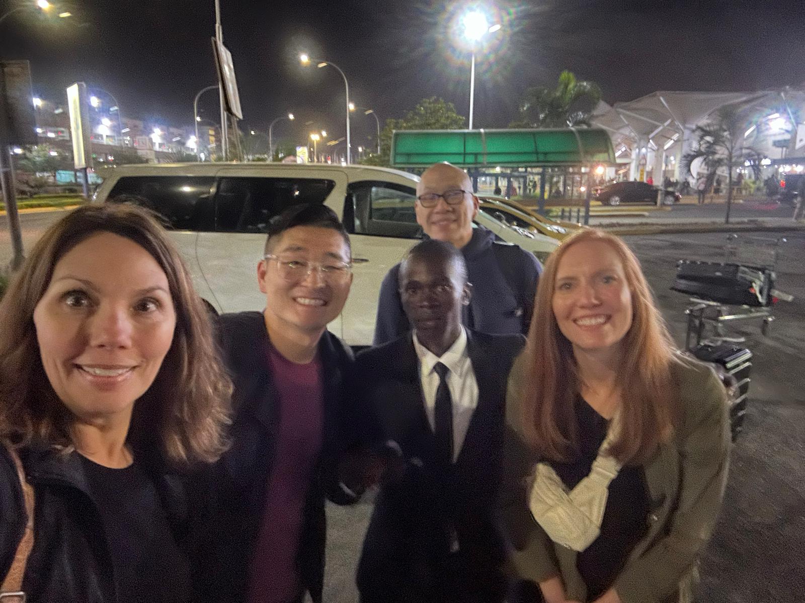 John meeting a group of arriving travellers at the airport at night